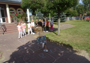 dzieci bawią się o ogrodzie przedszkolnym w piękny słoneczny dzień, grają w klasę reszta grzecznie czeka na swoją kolej